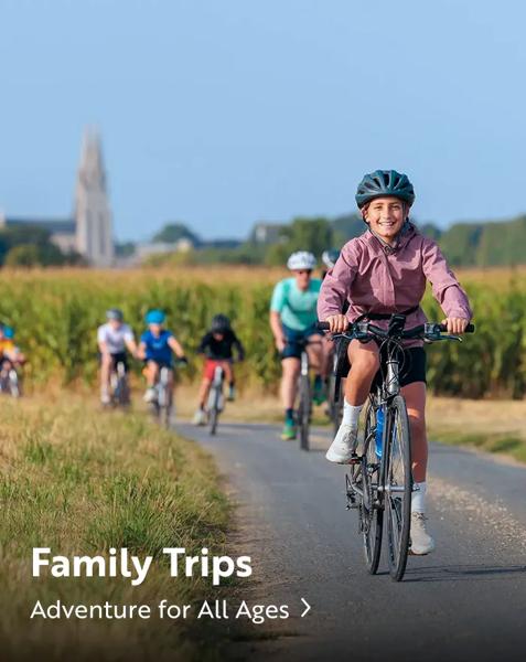 A family riding bicycles on a paved path through a rural field. Text overlay reads: "Family Trips. Adventure for All Ages".