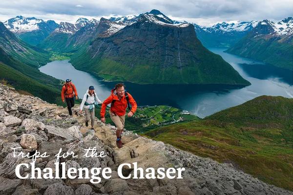 Three hikers on a mountain trail overlooking the Hjørundfjorden and the Sunnmøre Alps in Møre og Romsdal, Norway. Text overlay reads: Trips for the Challenge Chaser.