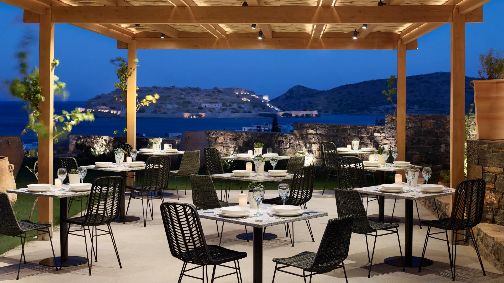 The Kelari Gourmet Restaurant at the Cayo Exclusive Resort & Spa in Crete, Greece, featuring a scenic, outdoor terrace overlooking Spinalonga island.
