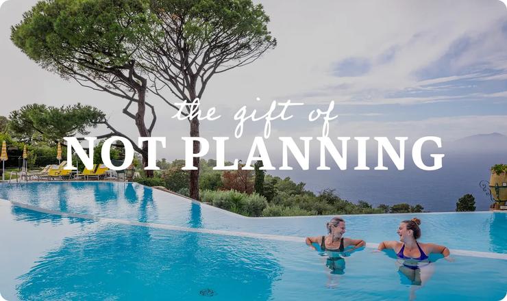 Two women relaxing in an infinity pool overlooking trees and the ocean, with the text "the gift of NOT PLANNING" overlaid in the center.