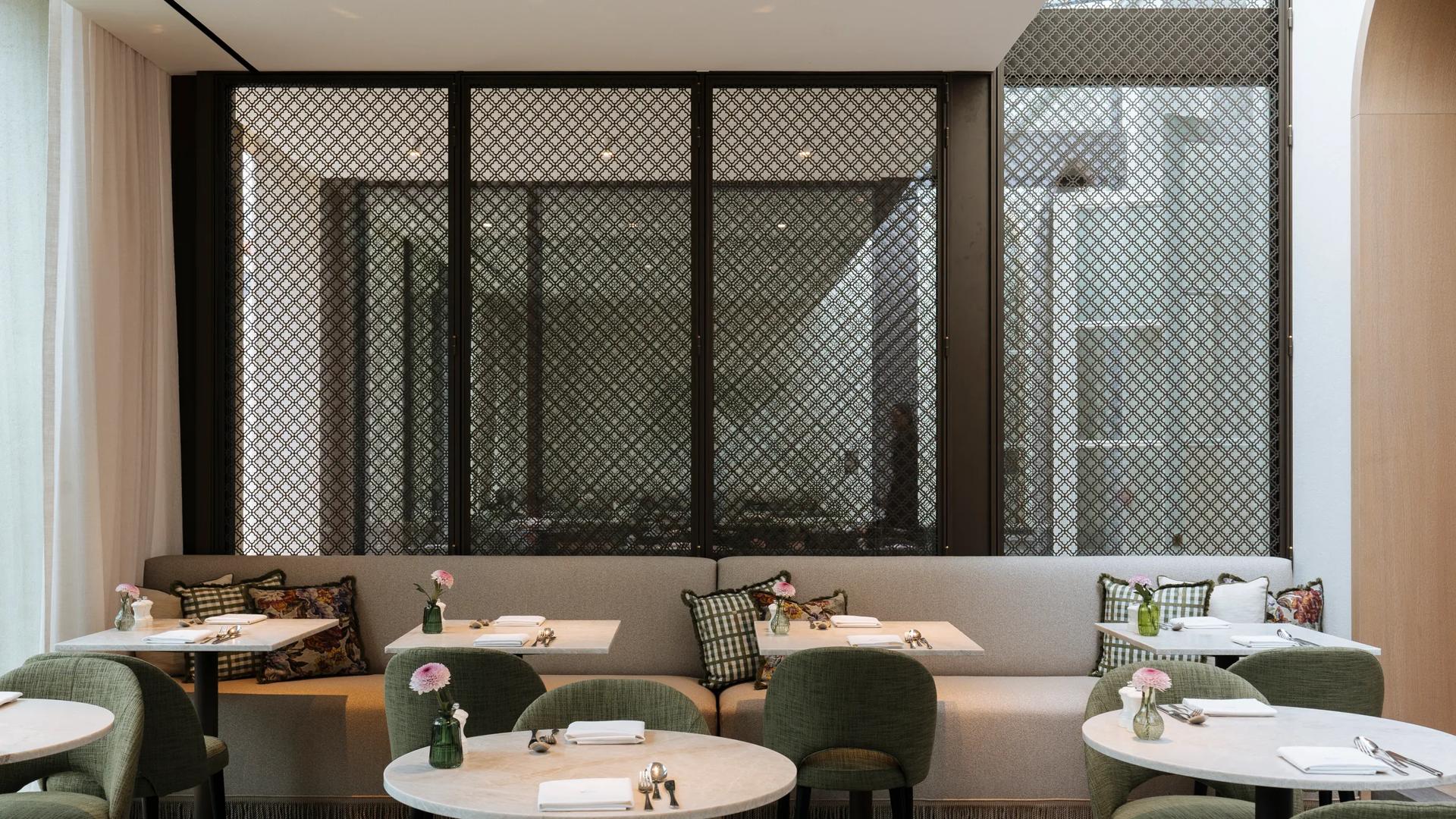 The restaurant area of the Hotel de Tuilerieen in Bruges, Belgium features green fabric dining chairs, marble round tables and comfortable bench seating.