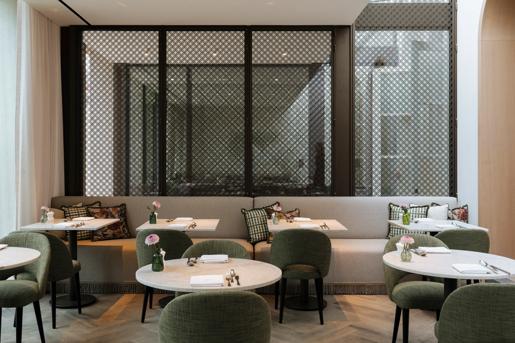 The restaurant area of the Hotel de Tuilerieen in Bruges, Belgium features green fabric dining chairs, marble round tables and comfortable bench seating.