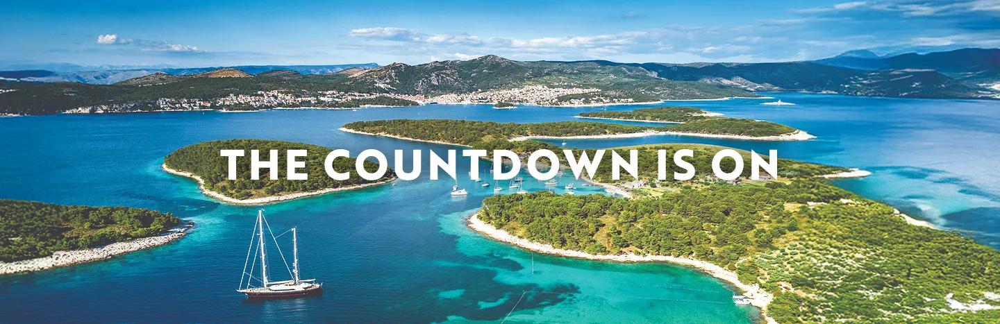 Pakleni Islands archipelago in the turquoise Adriatic Sea near Hvar, Croatia with several sailboats in the bay. Text overlay reads: "The countdown is on".