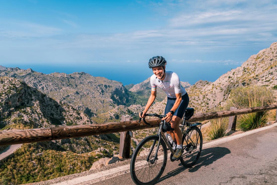 A bike rider smiles as he climbs a hill overlooking the ocean in Mallorca.