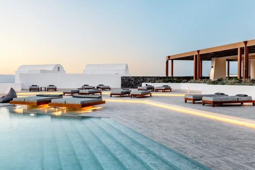 The outdoor pool terrace at the Santo Pure Oia Suites & Villas in Santorini, featuring minimalist wooden loungers and ambient lighting.