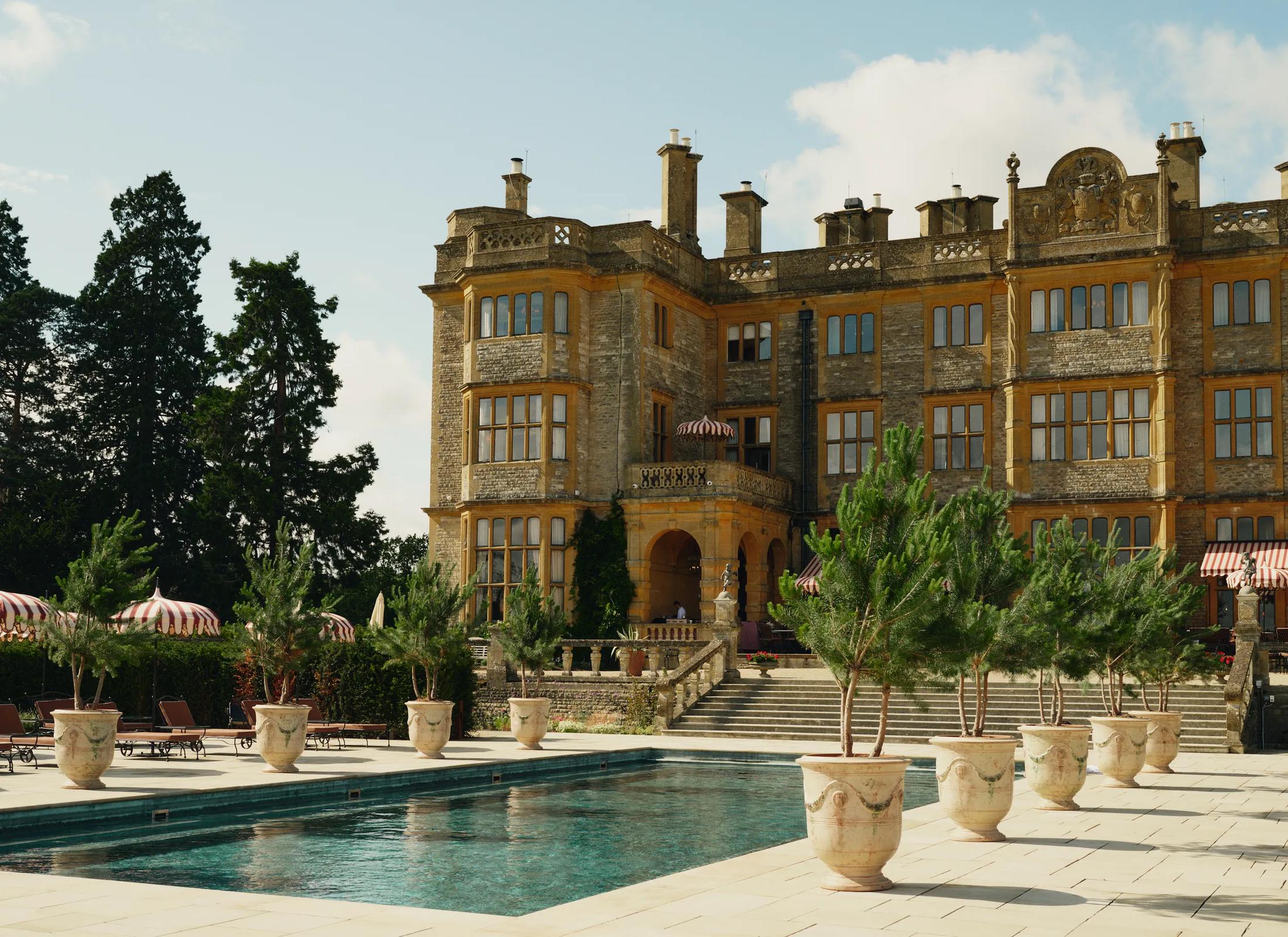 The South Terrace pool terrace and ornamental evergreens against the stone manor house at Estelle Manor in Oxfordshire, England.
