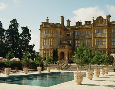 The South Terrace pool terrace and ornamental evergreens against the stone manor house at Estelle Manor in Oxfordshire, England.