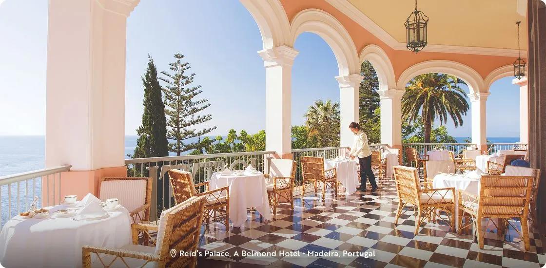 The famous outdoor dining terrace overlooking the ocean at Reid's Palace, A Belmond Hotel in Funchal, Madeira, Portugal that features classic black-and-white checkered tiled floor and tall white architectural arches.