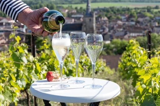 Pouring and tasting of dry sparkling wine brut, grand reserve, champagne in Ay-Champagne on green hilly vineyards and viewon old wine making village in Vallee de la Marne, Champagne region, France.