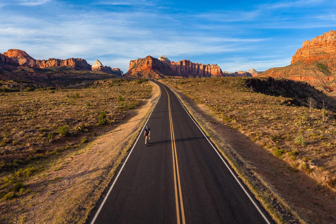 A smooth, empty highway in Utah in the late afternoon with the sun highlighting the red rock surroundings.