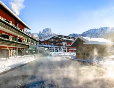 The heated outdoor pool with rising steam in winter, set against the traditional Alpine chalet architecture at the Alpenroyal Hotel in Selva di Val Gardena, Italy.