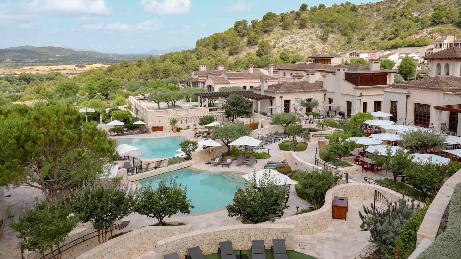 Elevated view of the Cap Vermell Grand Hotel resort complex featuring terraced swimming pools, patio dining under white umbrellas, and hillside vistas.