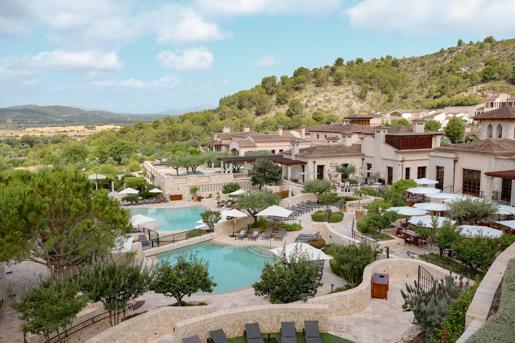 Elevated view of the Cap Vermell Grand Hotel resort complex featuring terraced swimming pools, patio dining under white umbrellas, and hillside vistas.
