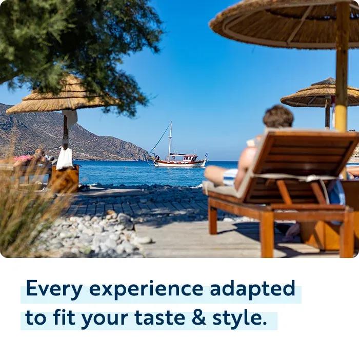 Alt Text: A person relaxing on a wooden lounge chair under a thatched beach umbrella on a sunny day, looking out toward a blue sea with a sailboat anchored offshore. Below the image, dark blue text with light blue highlighting reads "Every experience adapted to fit your taste & style."
