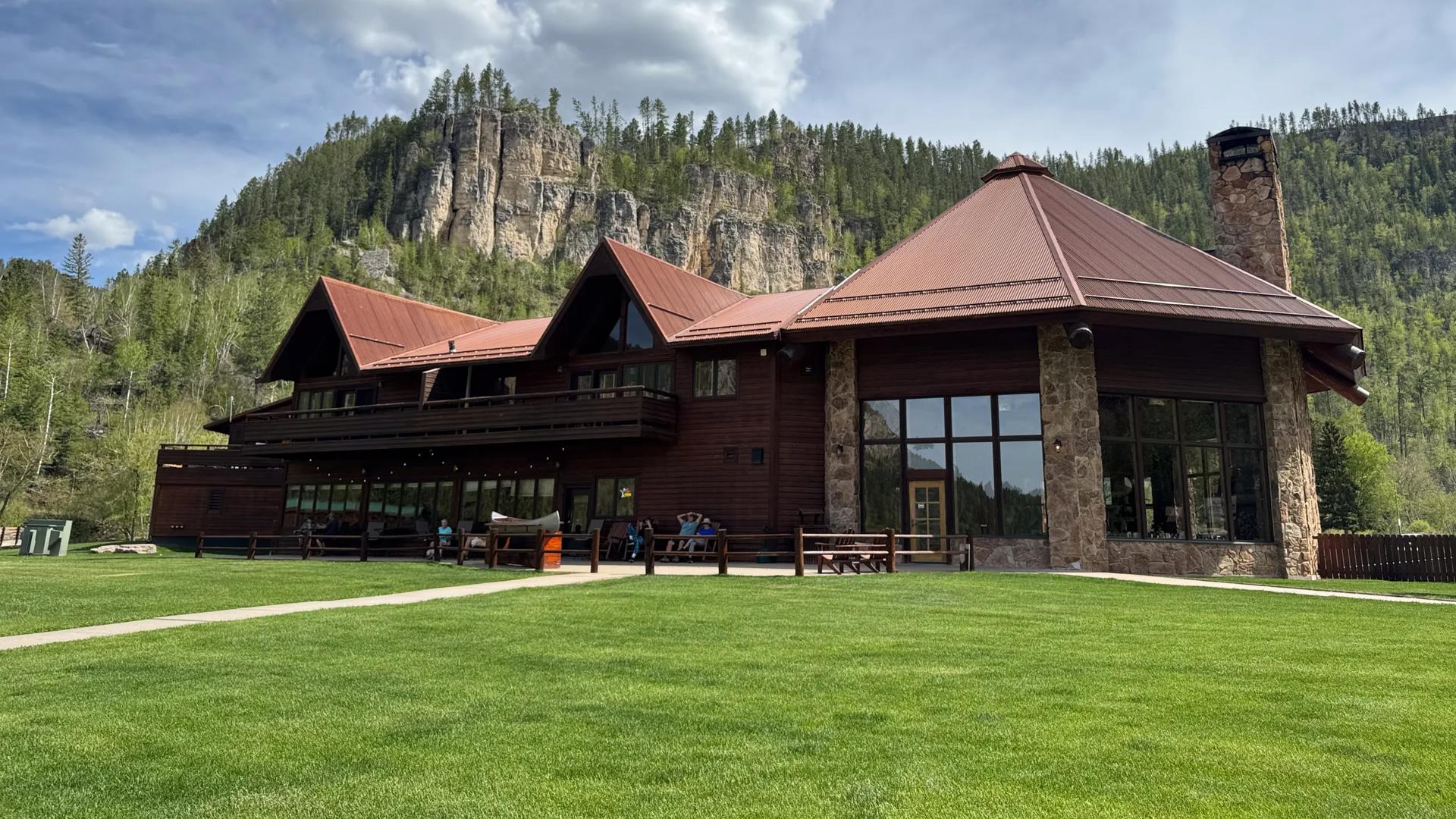 The spearfish canyon Lodge in Lead exterior. Big floor to ceiling windows and a mountainous backdrop can be seen encapsulating this rustic building.