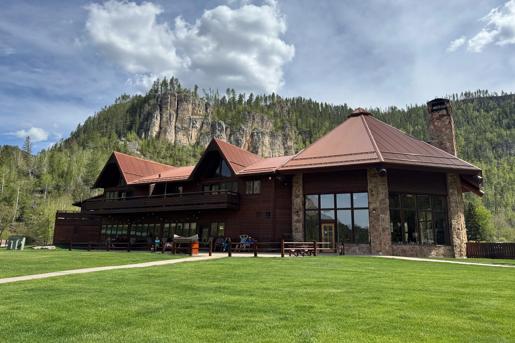 The spearfish canyon Lodge in Lead exterior. Big floor to ceiling windows and a mountainous backdrop can be seen encapsulating this rustic building.