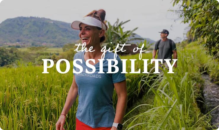 A smiling woman walking through a lush green field with mountains in the background, with the text "the gift of POSSIBILITY" overlaid in the center.