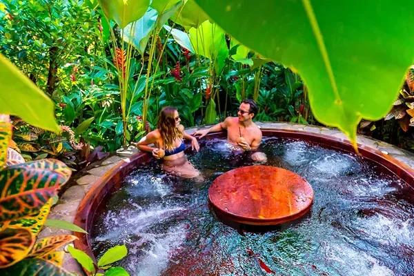 A couple relaxing in a hot tub surrounded by a lush tropical rainforest at Nayara Gardens near the Arenal Volcano in La Fortuna, Costa Rica.
