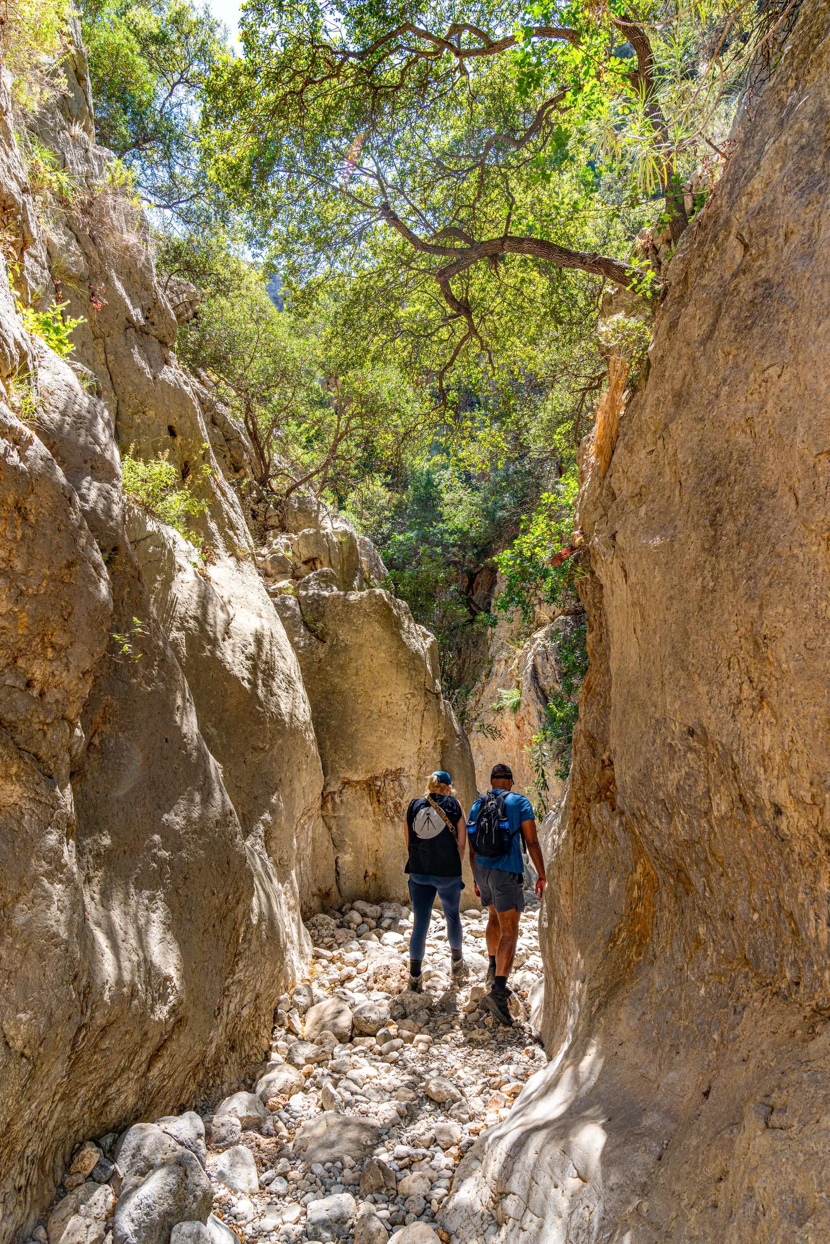 Two guests hike a narrow, rocky trail of the Kritsa Gorge in Crete, Greece.