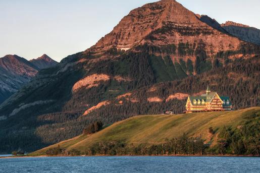 The Prince of Wales Hotel located in Waterton Lakes National Park, Alberta, Canada is seen from a distance, overlooking Upper Waterton Lake with a mountain range in the background.