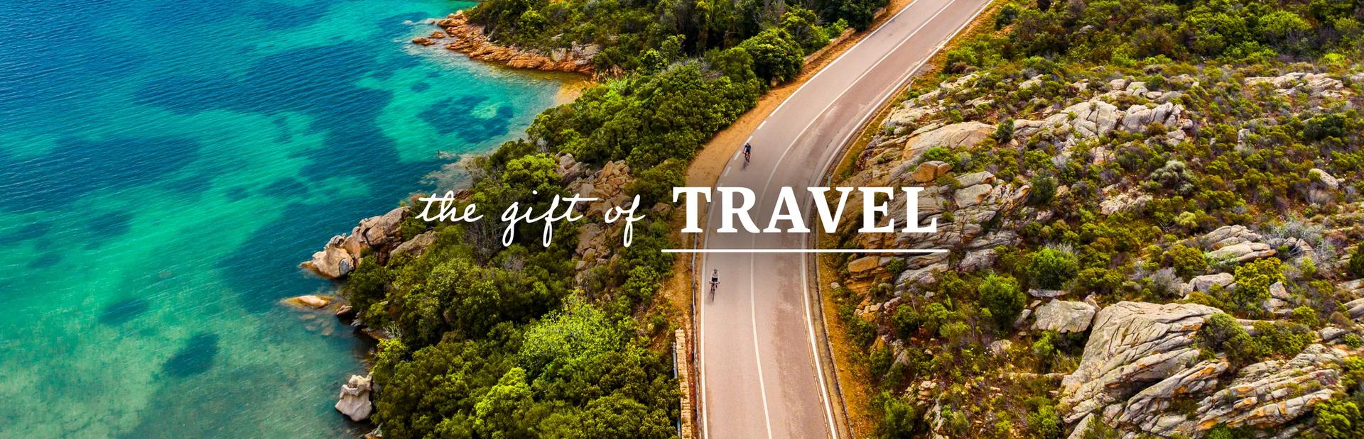 A coastal road winding along the turquoise waters and granite hills of Sardinia, Italy. Text overlay reads: The gift of travel. 