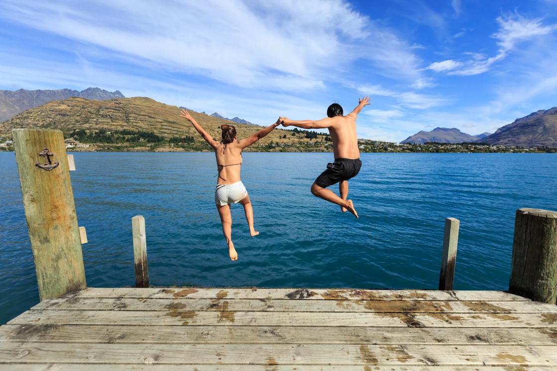 Young couple jumping on the edge of a dock into the Lake Wakatipu.