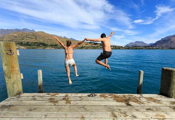 Young couple jumping on the edge of a dock into the Lake Wakatipu.