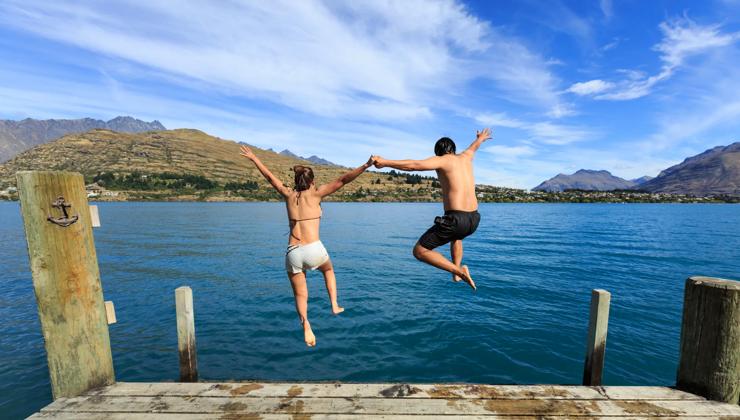 Young couple jumping on the edge of a dock into the Lake Wakatipu.