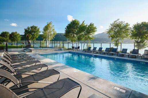 An outdoor swimming pool and hot tub area lined with lounge chairs at the Hood River Inn, overlooking a river and bridge on a sunny day.